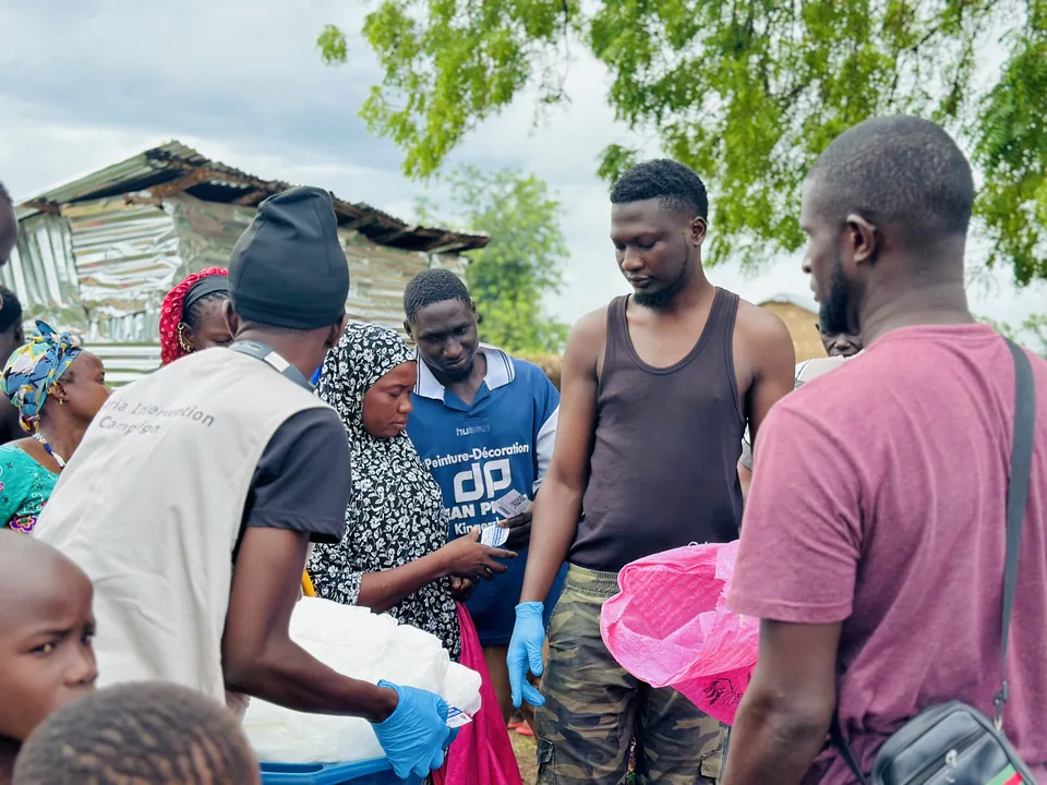 A campaign team in gloves and vests checking a card and handing out nets in a village